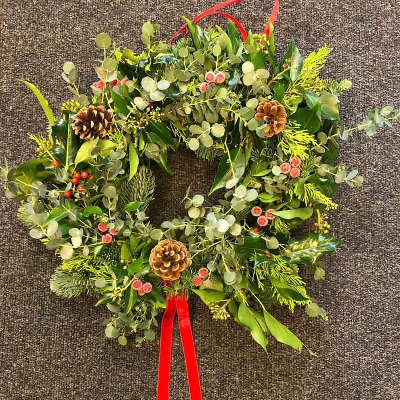 A finished Christmas wreath with decorations and a red bow.