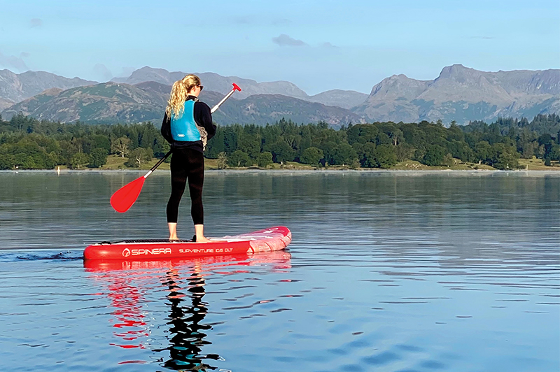 Paddle boarder on lake Windermere stood looking at the view.